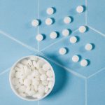 A bowl filled with white mint tablets is placed on a blue surface, alongside several scattered mint tablets.