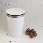 A white reusable coffee cup with a silver band at the top, alongside some brown candies.