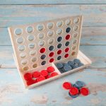 A Connect Four game featuring a beige game board with red and gray discs, set on a blue wooden surface.