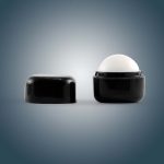 A black cube-shaped lip balm container with a removable lid, featuring a rounded white balm inside.