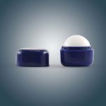 A cube-shaped lip balm in a navy blue container, featuring a removable cap and a white balm inside.