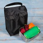 A black Sumo Cooler Lunch Bag sits beside a lunch container filled with fruits and a green drink can.