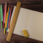 A bamboo 30cm ruler rests on lined paper, accompanied by colourful pens and a yellow eraser.