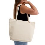 A cream-coloured tote bag with rope handles, held by a woman wearing a black top.