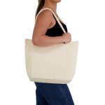 A cream-coloured canvas tote bag with rope handles, held by a person in a black top and blue jeans.