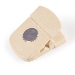 A beige magnetic clip with a textured grip and silver circular accent, featuring a logo.