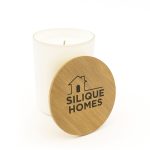 A medium-sized glass candle with a wooden lid, featuring a logo on the lid and a white wax interior.