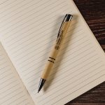 A pen with a kraft paper barrel and black accents rests atop an open lined notebook.