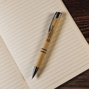A pen with a kraft paper barrel and black accents rests atop an open lined notebook.