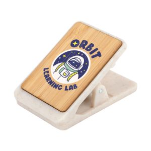 A bamboo magnetic clip with a design featuring an astronaut surrounded by stars, set on a speckled white base.