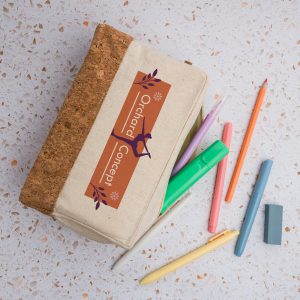 A cork and beige utility case with colorful pens and pencils scattered around it. The case has a logo on it.