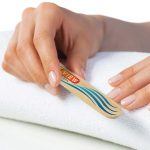 A bamboo nail file with a logo, resting on a white towel, held by a hand with manicured nails.