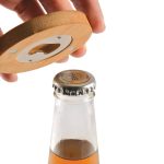 A drink bottle opener coaster made of bamboo, with a circular design and a bottle cap opening mechanism.
