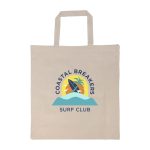 A beige tote bag with a logo featuring surfboards, palm trees, and waves in blue and yellow tones.