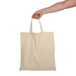 A hand holds a natural-coloured tote bag with short handles, featuring a plain design and no visible branding.