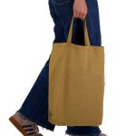 A person holding a mustard yellow reusable tote bag with short handles, dressed in denim.