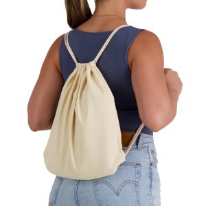 A cream-coloured drawstring backpack is worn on the back of a person, featuring simple cord straps and a gathered top.