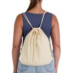 A cream-coloured drawstring backpack is worn on the back of a person, showcasing its simple design and straps.