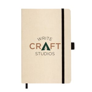 A beige A5 notebook with a black elastic band and a logo featuring the words "WRITE CRAFT STUDIOS."