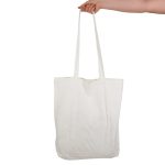 A white tote bag with long handles, held by a hand, featuring a logo.