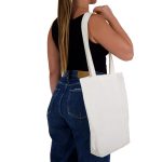 A white tote bag with long handles is being held by a person wearing a black top and blue jeans.