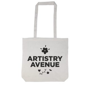 A tote bag with a long handle featuring the text "ARTISTRY AVENUE" and decorative floral elements.