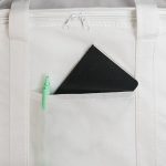 A black notebook and green pen are visible in a front pocket of a white cooler bag. The bag features a zippered closure.