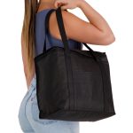 A black cooler bag with sturdy handles, carried by a person in a casual outfit. The bag features a logo.