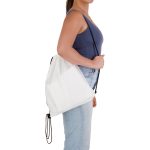A white drawstring backpack is held by a person wearing a blue top and jeans, featuring a simple design with a logo.