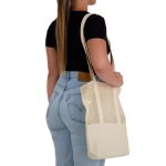 A tote bag in cream with a mesh design is held by a person wearing a black top and blue jeans.