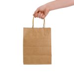 A medium brown paper bag with twine handles held by a hand. The bag has a simple design and no visible logos.