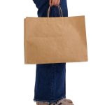 A large brown paper bag with handles, held by a person wearing jeans and shoes. It features a simple design.