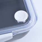 A black food container with a clear lid and a white pull tab for easy opening. It features a logo on the side.