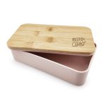 A pink lunch box with a bamboo lid and an engraved logo, featuring a divided interior.