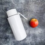 A drink bottle in sleek white stainless steel with a removable straw, accompanied by a red apple.
