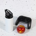 A drink bottle featuring a flip straw lid, alongside a red apple and a black gaming controller.