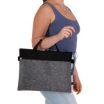 A grey felt satchel with black accents, held by a person wearing a blue top and light jeans. It has a logo.