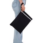 A black Cosi Wet Bag is held by a person wearing light-wash jeans, featuring a white zip and a sturdy handle.
