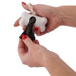 A bone-shaped dog waste bag dispenser in white, being loaded with a black waste bag, held by two hands.