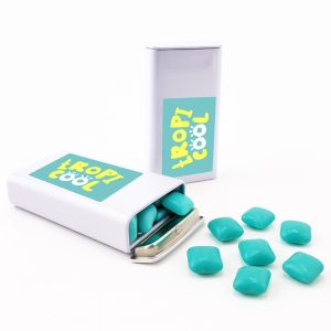 A pack of turquoise chewy mints, with some mints spilled out, in a silver tin featuring a logo.