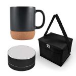 A black coffee mug with a cork base, a black speaker, and a black carrying bag with a strap.