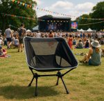 A black folding chair with a mesh backrest set against a vibrant outdoor festival scene.