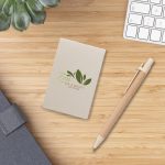 A beige sticky note pad featuring a green leaf logo, alongside a wooden pen, on a wooden surface.