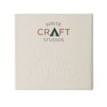 A square, off-white notepad with subtle embossed text, featuring a logo and made from recycled materials.