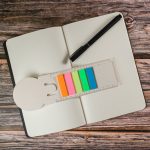 A milk carton-shaped bookmark in light beige with colorful post-it flags in pink, orange, yellow, green, and blue.
