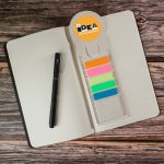 A Circle Milk Carton Bookmark in pastel colors with a ruler, placed on a dotted notebook alongside a black pen.