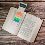 A rectangular bookmark in pastel colours rests in an opened book, featuring a logo at the top.