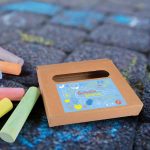 A box of Sketch Pavement Chalk in various colors, with a whimsical design on the front, placed on a textured surface.