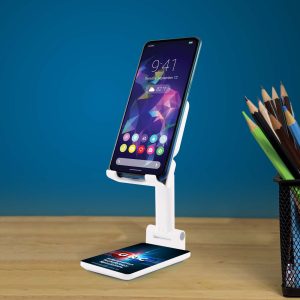 A white phone stand holds a smartphone against a blue background, positioned on a wooden surface next to a pencil holder.