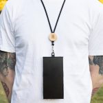 A phone neck lanyard featuring a wooden clip and a black strap, securely holding a smartphone.